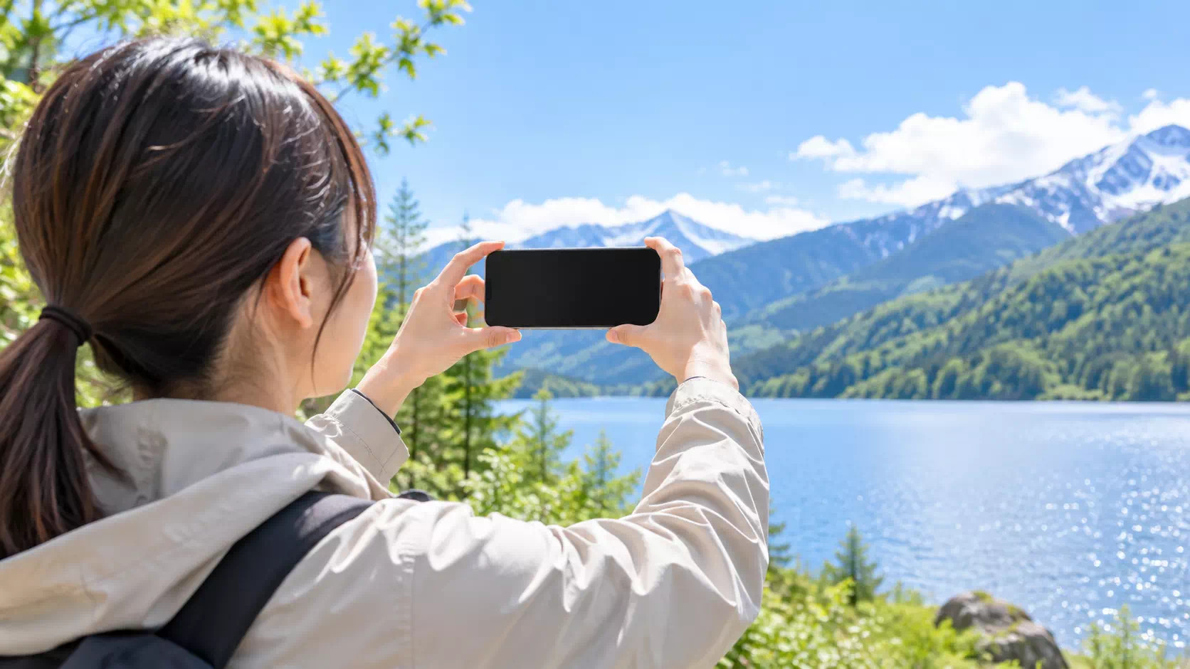広い山と湖の景色をスマートフォンで撮影しようとしている人の後ろ姿